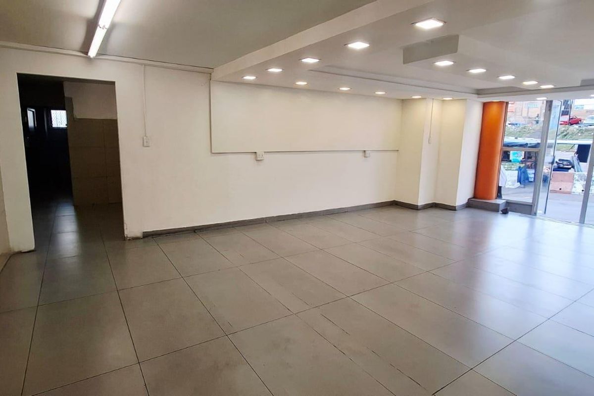 A spacious, vacant commercial office or retail space featuring large glass windows, tiled flooring, and a mix of recessed and strip lighting.