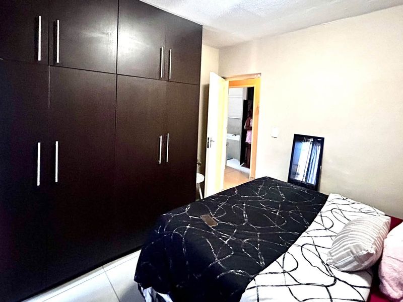 A bedroom featuring dark wood built-in cupboards and tiled flooring, with an adjacent doorway leading to another room.