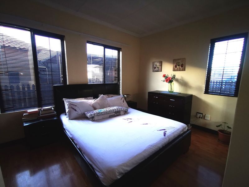A well-lit bedroom featuring laminate flooring, multiple windows with fitted venetian blinds, and neutral wall finishes.