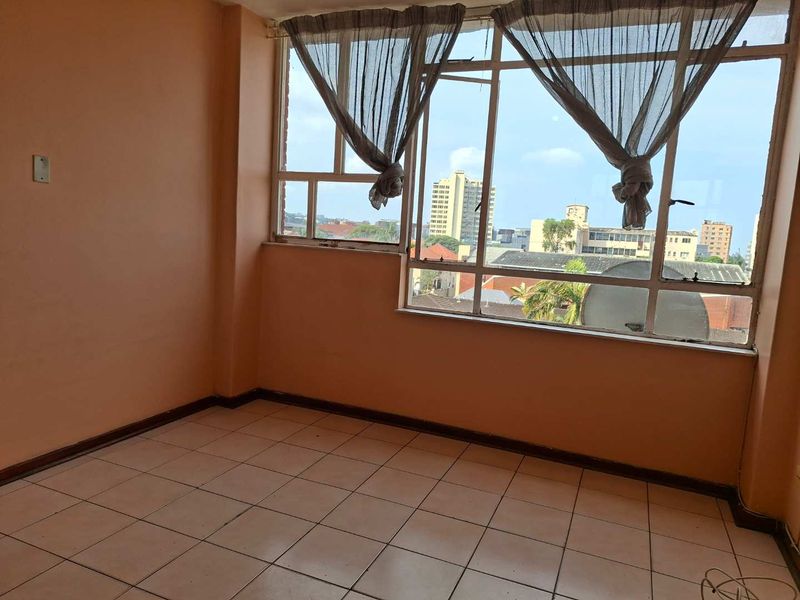 An empty living room featuring tiled flooring and large metal-framed windows with an urban city view.