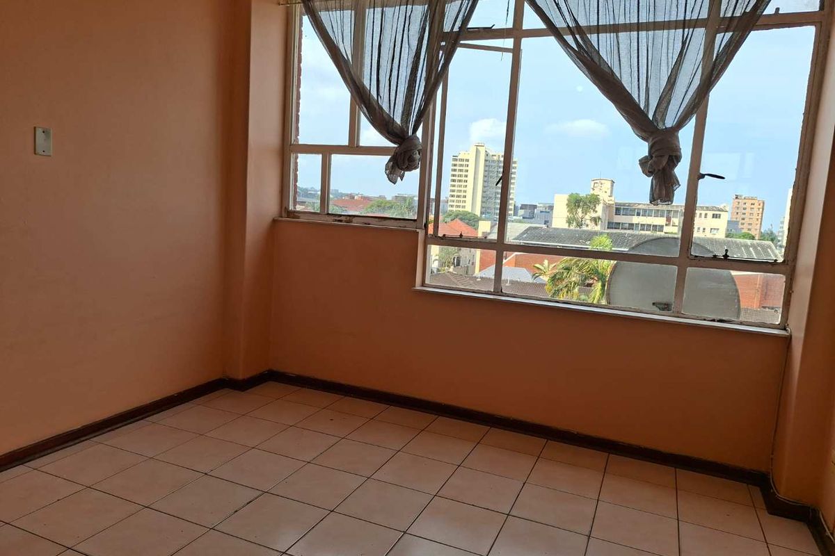 An empty living room featuring tiled flooring and large metal-framed windows with an urban city view.