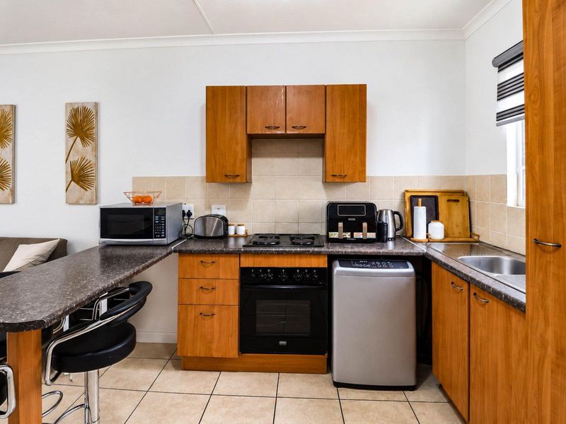 A functional kitchen featuring wood-look laminate cabinetry, dark countertops, a built-in oven with gas hob, and neutral tiled flooring.