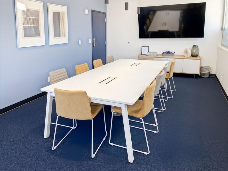 A modern, well-maintained office meeting room featuring blue accent walls, carpeted flooring, and a wall-mounted display screen.