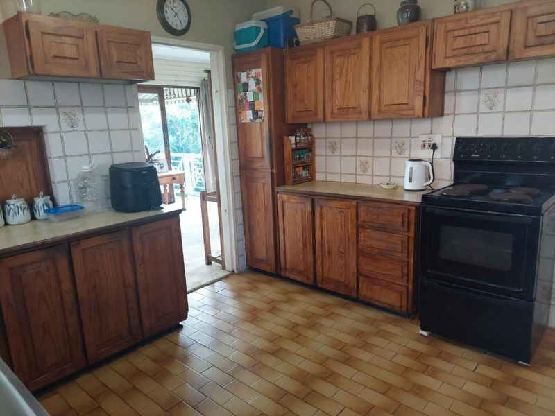 A dated kitchen featuring traditional wooden cabinetry, tiled backsplash, and a freestanding electric stove, with direct access to an outdoor patio area.