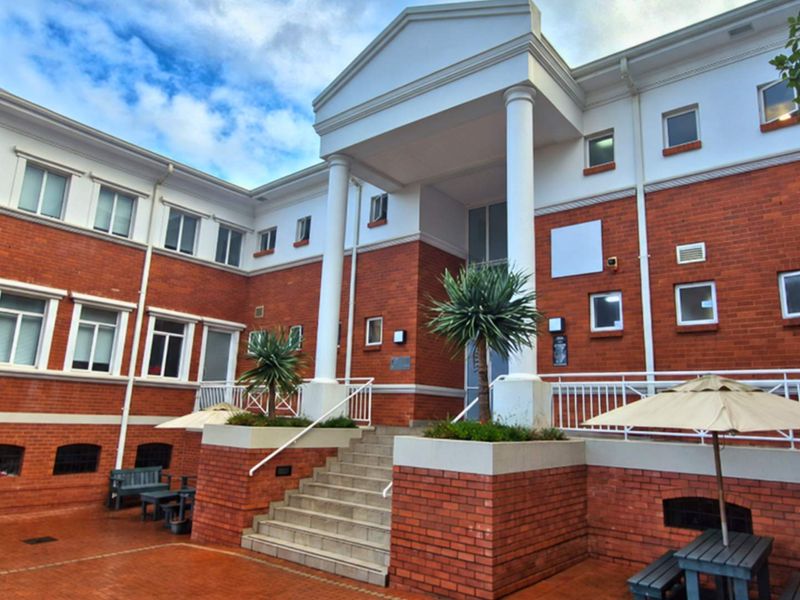 A professional office building exterior featuring a classic brick facade, prominent columns, and a welcoming paved entrance courtyard with stairs.