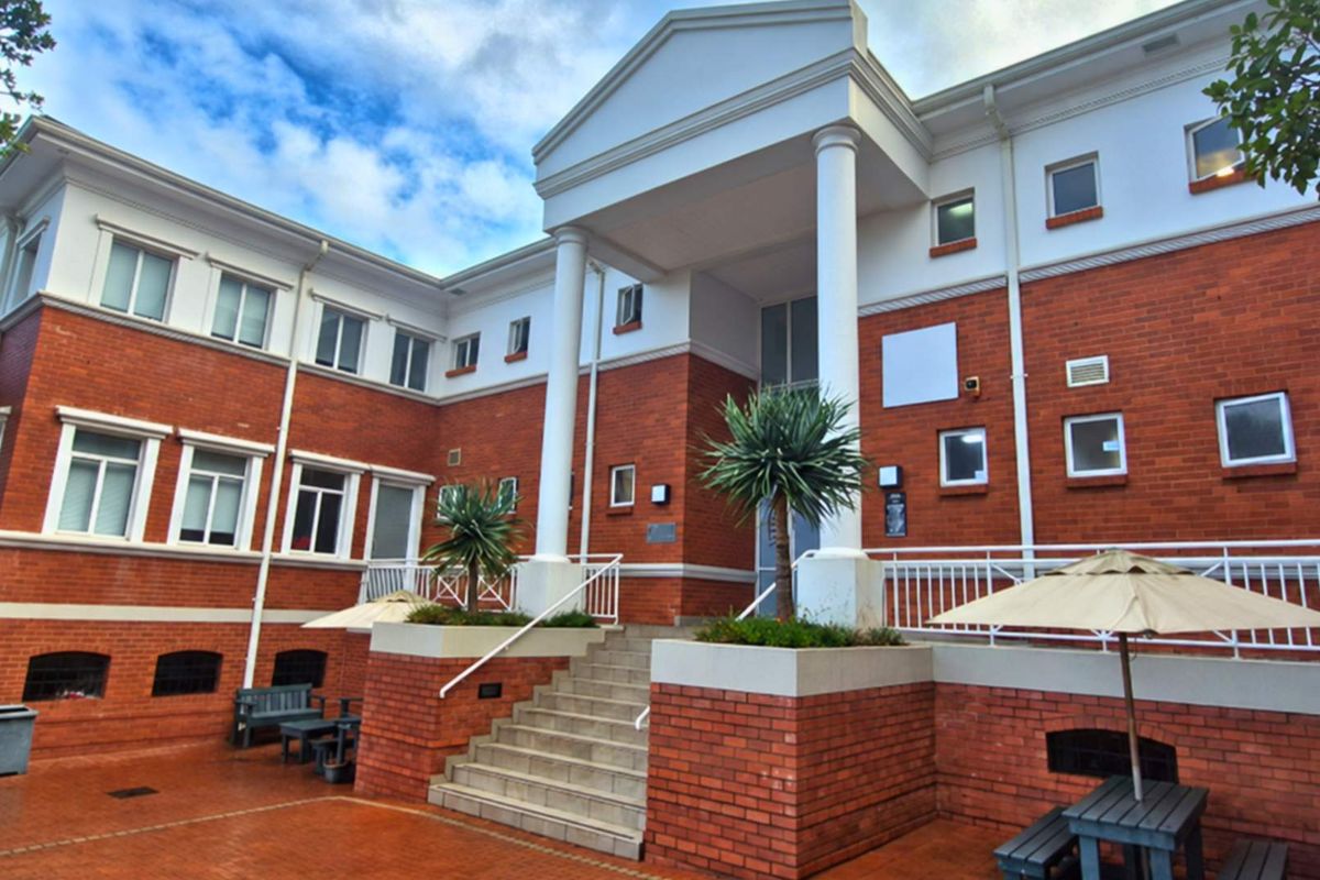 A professional office building exterior featuring a classic brick facade, prominent columns, and a welcoming paved entrance courtyard with stairs.