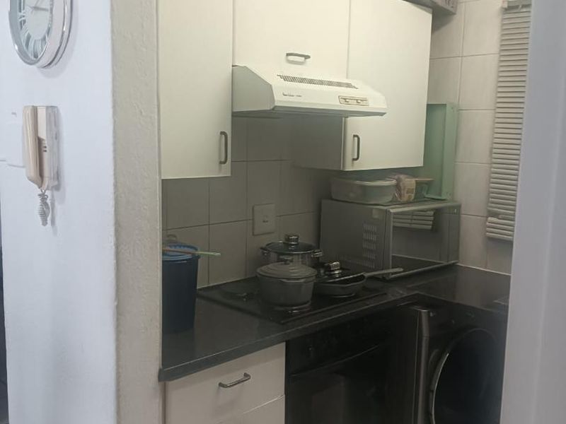 Compact kitchen featuring white cabinetry, built-in oven, electric hob, extractor fan, and tiled splashback, providing essential cooking and laundry utility space.