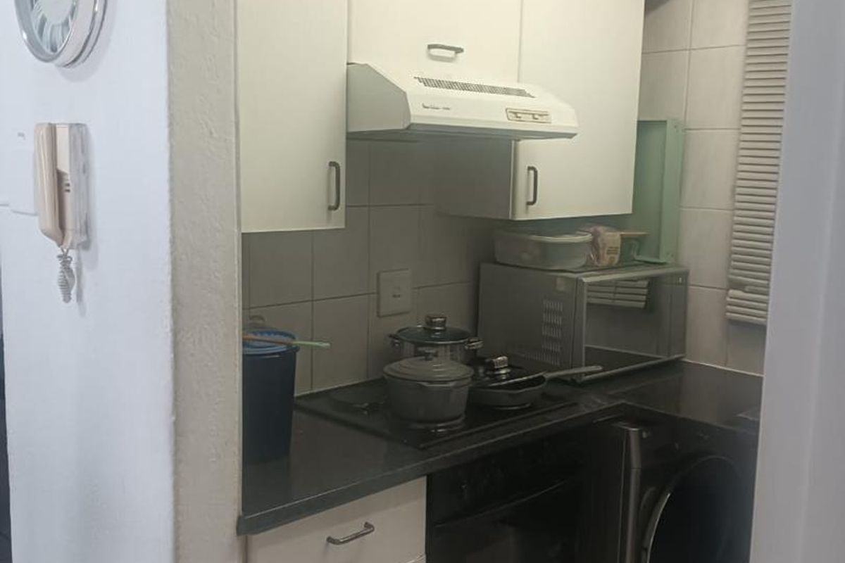 Compact kitchen featuring white cabinetry, built-in oven, electric hob, extractor fan, and tiled splashback, providing essential cooking and laundry utility space.