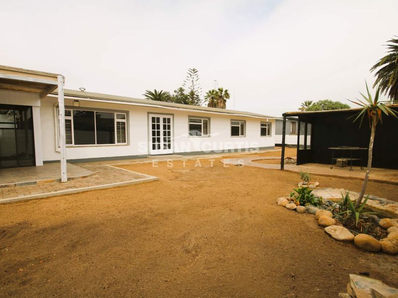 Rear view of the property featuring a covered patio, paved pathways, and a large, open yard area with potential for landscaping.