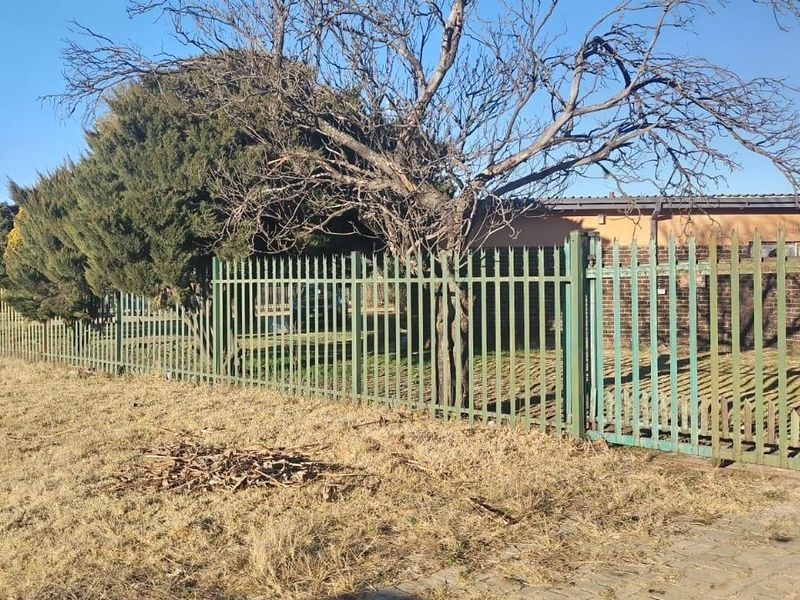 Front view of the property featuring steel palisade fencing and a paved driveway area.