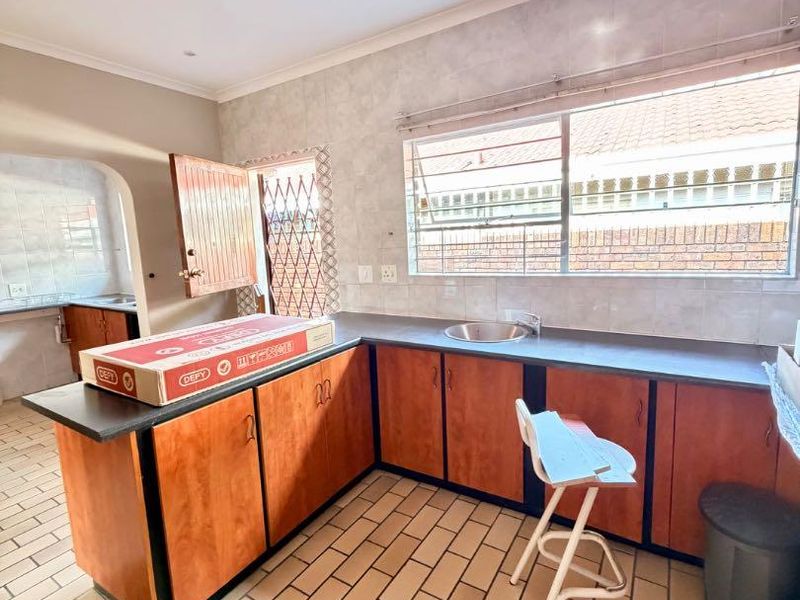 Kitchen featuring l-shaped cabinetry, laminate countertops, stainless steel sink, and tiled flooring with a view towards an adjacent scullery area.