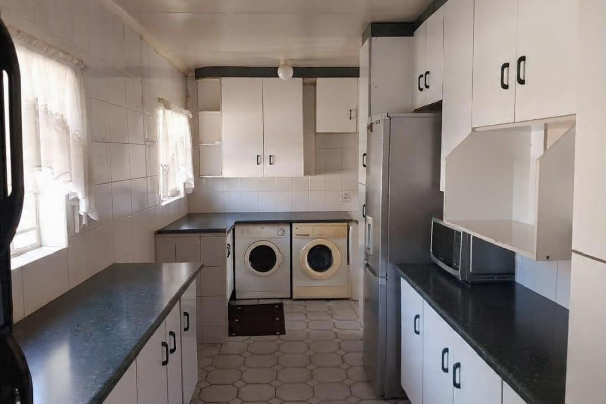 Functional kitchen featuring white cabinetry, dark countertops, tiled walls, and integrated laundry appliance space.