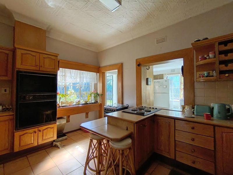 A dated kitchen featuring wooden cabinetry, built-in oven, electric hob, and a unique pressed metal ceiling with a convenient pass-through window.
