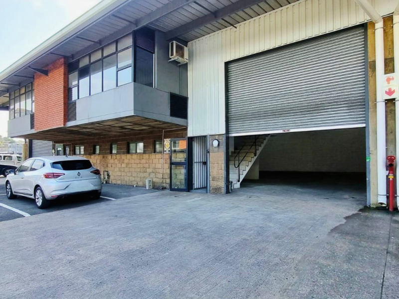 Industrial property exterior featuring a large roller shutter door, brick and metal cladding, and dedicated parking space.