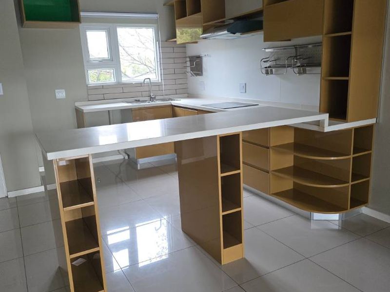 Modern kitchen featuring high-gloss cabinetry, quartz countertops, integrated hob, extractor fan, and sleek tiled flooring in an open-plan layout.