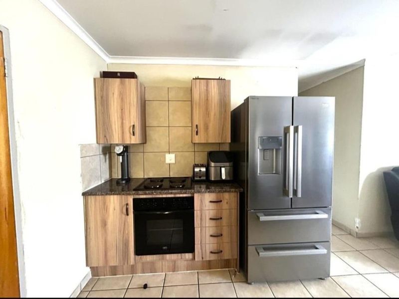 Compact kitchen featuring wood-finish cabinetry, granite countertops, tiled backsplash, and built-in oven with gas hob.
