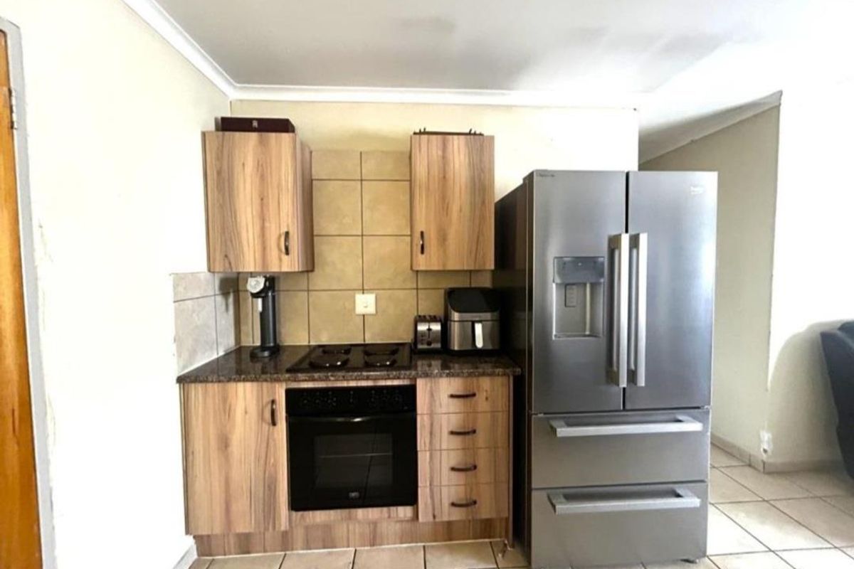 Compact kitchen featuring wood-finish cabinetry, granite countertops, tiled backsplash, and built-in oven with gas hob.