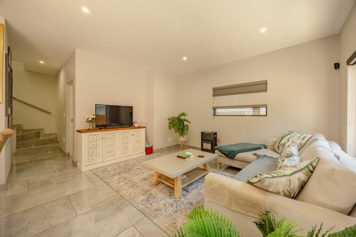A bright and modern living room featuring tiled flooring, recessed downlighting, and an adjacent staircase with a sleek metal handrail.