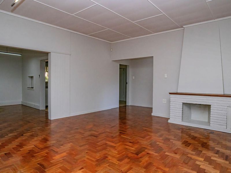 Spacious living area featuring classic herringbone parquet flooring and a traditional brick fireplace, offering a versatile blank canvas for interior design.