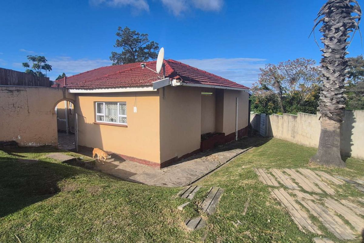 Rear view of the property featuring a tiled roof, boundary walls, and a garden area with concrete paving.