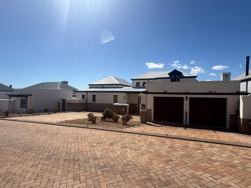 Front exterior view of the property featuring a double garage, paved driveway, and stone-clad accents under a metal roof.