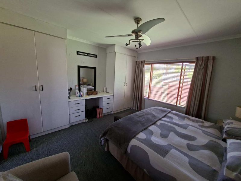 Spacious bedroom featuring built-in cupboards, a integrated vanity unit, ceiling fan, and large window with venetian blinds.