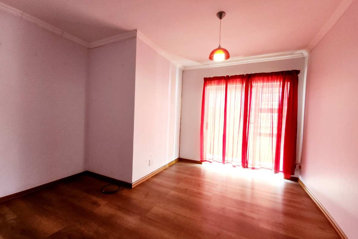 A bright, empty living room featuring laminate wood flooring, crown molding, and sliding glass doors with red curtains.