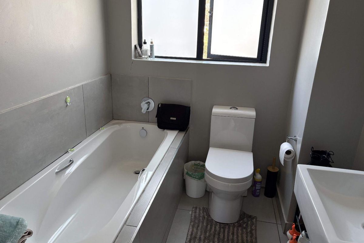 A functional bathroom featuring a bathtub, toilet, and basin with neutral wall tiles and tiled flooring, requiring minor cosmetic attention to the wall.