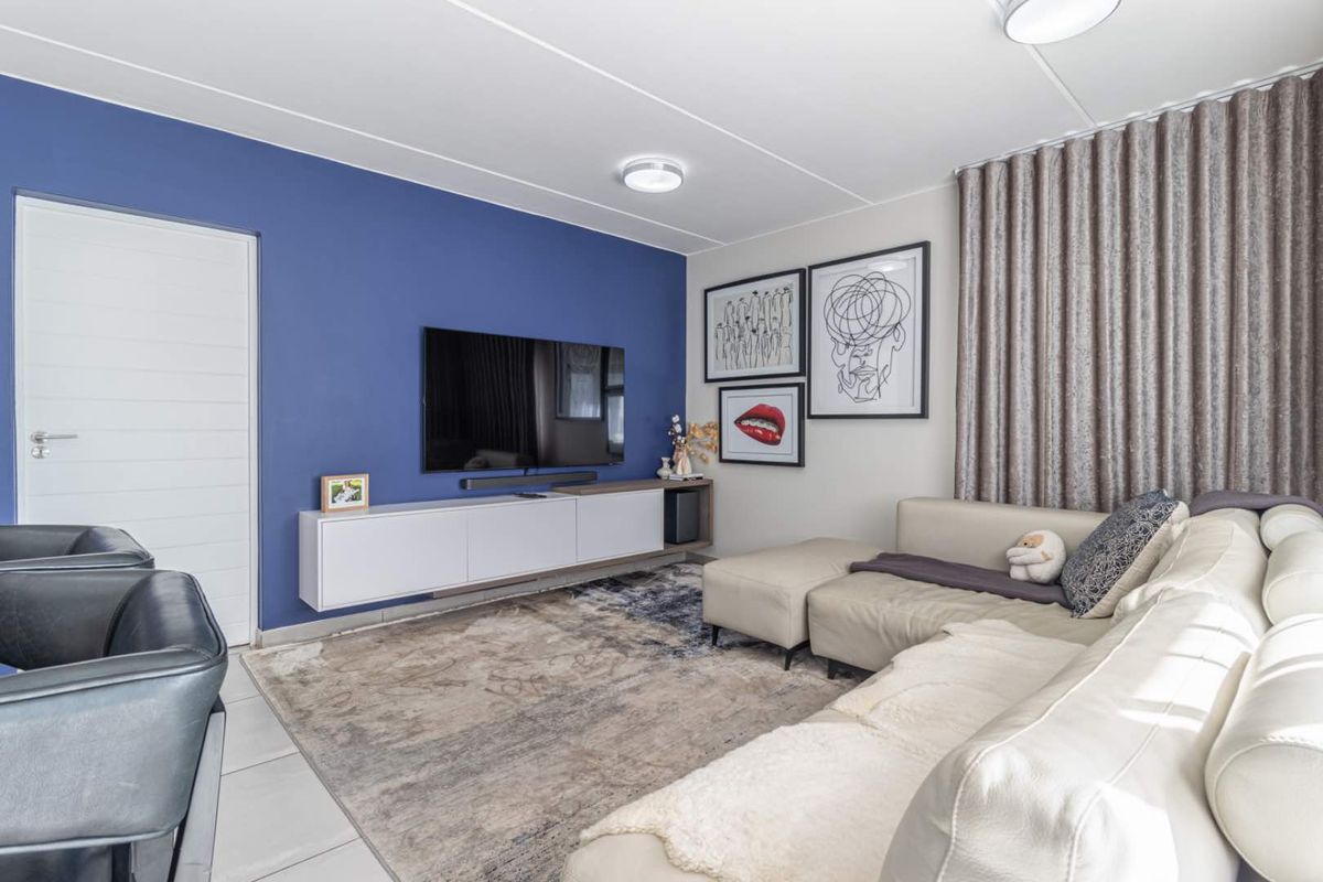 A well-maintained living room featuring a bold blue accent wall, tiled flooring, and a modern floating media console.