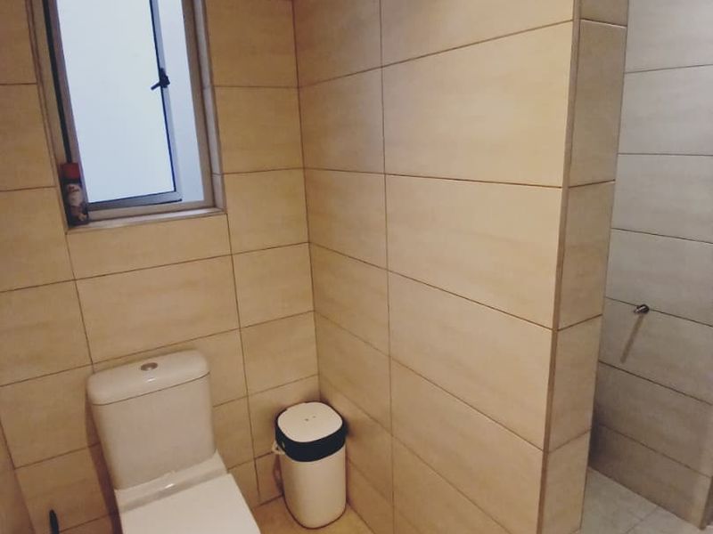 A modern bathroom featuring neutral ceramic wall and floor tiles, a white toilet, and a tiled partition wall separating the shower area.