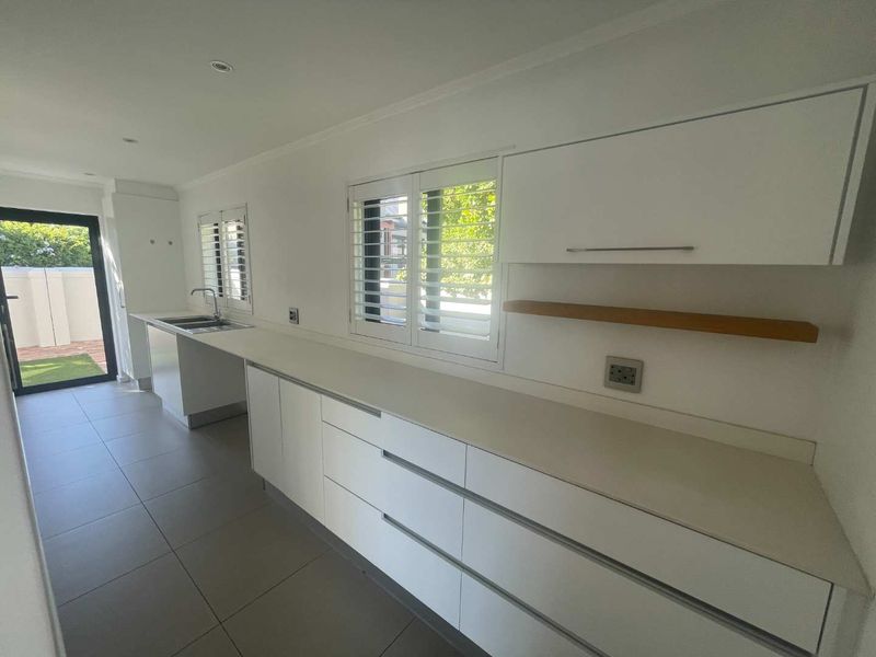 A clean, modern kitchen featuring white cabinetry, stone countertops, tiled flooring, and plantation shutters, offering a bright and functional workspace.