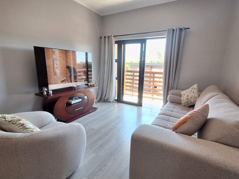 A well-maintained living room featuring light-toned laminate flooring and a sliding glass door providing direct access to a private balcony.