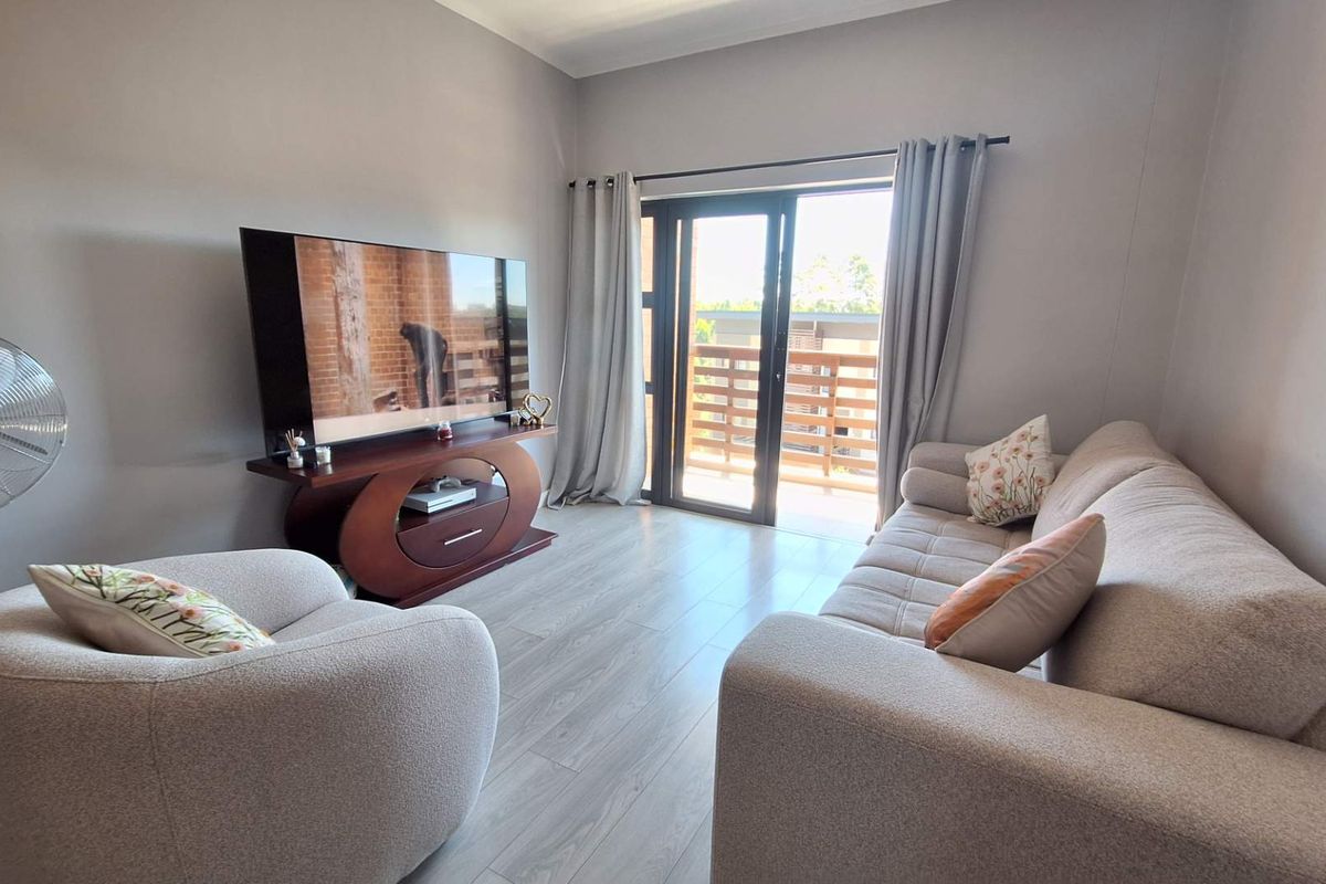 A well-maintained living room featuring light-toned laminate flooring and a sliding glass door providing direct access to a private balcony.