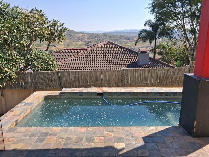Outdoor pool area featuring stone tiling and scenic hillside views, enclosed by reed fencing.