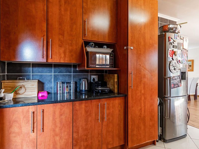 A functional kitchen featuring warm-toned wooden cabinetry, dark granite countertops, and a tiled backsplash, seamlessly flowing into the adjacent living area.
