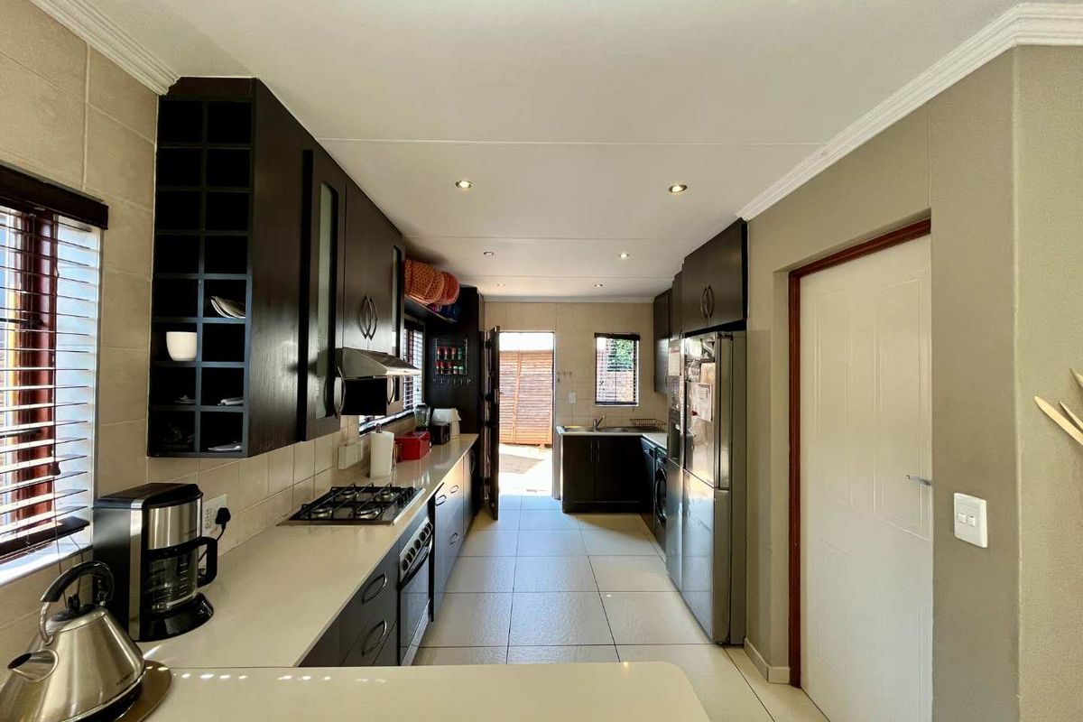 A functional galley-style kitchen featuring dark cabinetry, stone countertops, a gas hob, and tiled flooring with direct access to the rear exterior.