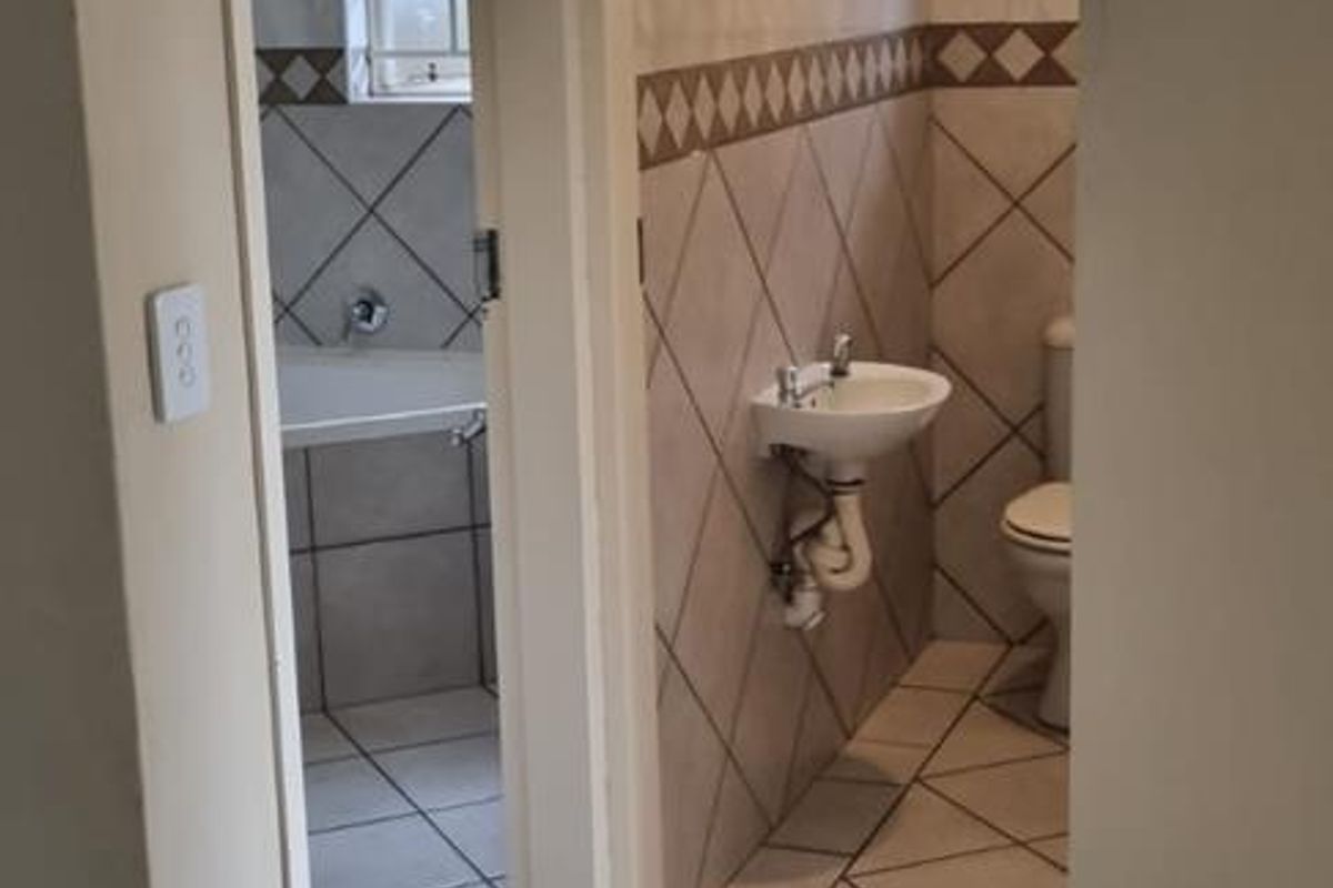 A dated bathroom featuring tiled walls and floors, a pedestal basin, and a toilet, requiring cosmetic updates to improve its overall condition.