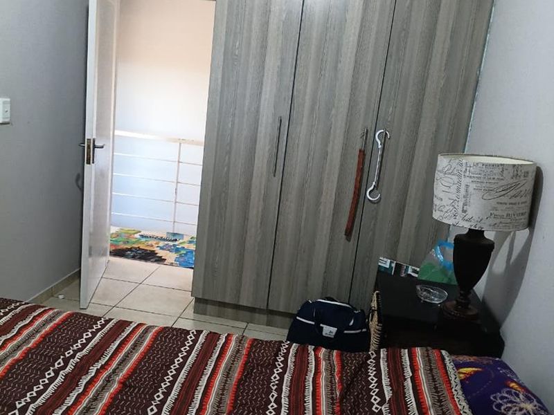 A bedroom featuring built-in wood-grain wardrobes and tiled flooring, with an open doorway leading to an adjacent area.