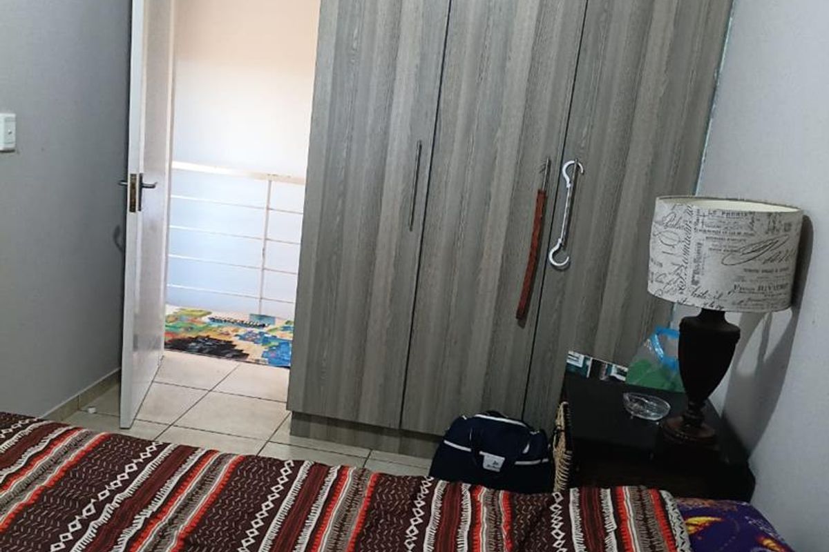 A bedroom featuring built-in wood-grain wardrobes and tiled flooring, with an open doorway leading to an adjacent area.