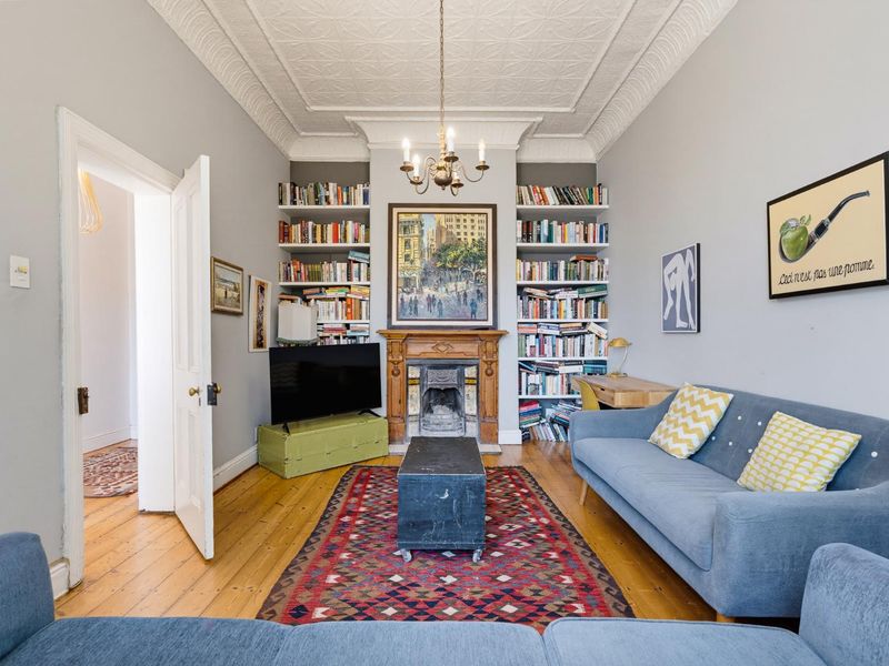 A well-maintained living room featuring original ornate ceiling details, built-in bookshelves, a classic timber fireplace mantel, and polished hardwood flooring.