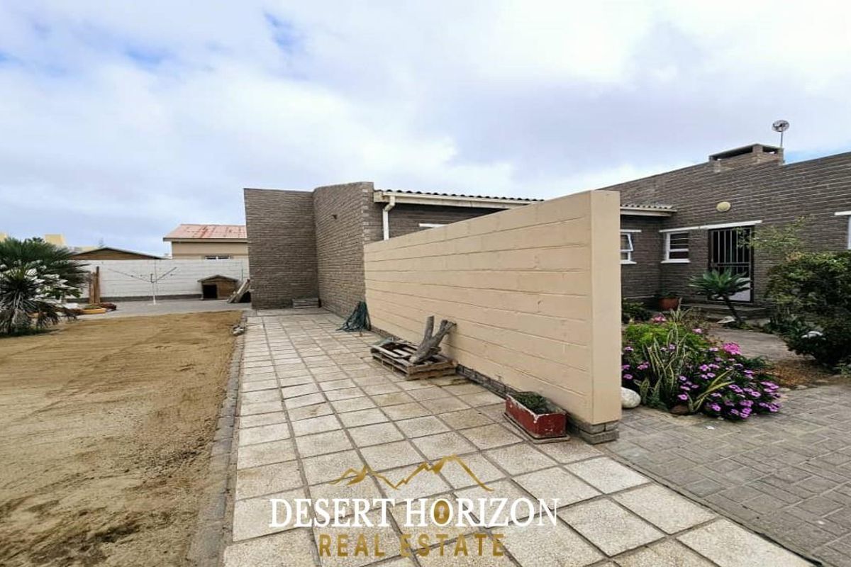 A rear exterior view of the property featuring a paved patio area, a low privacy wall, and an adjacent garden space.