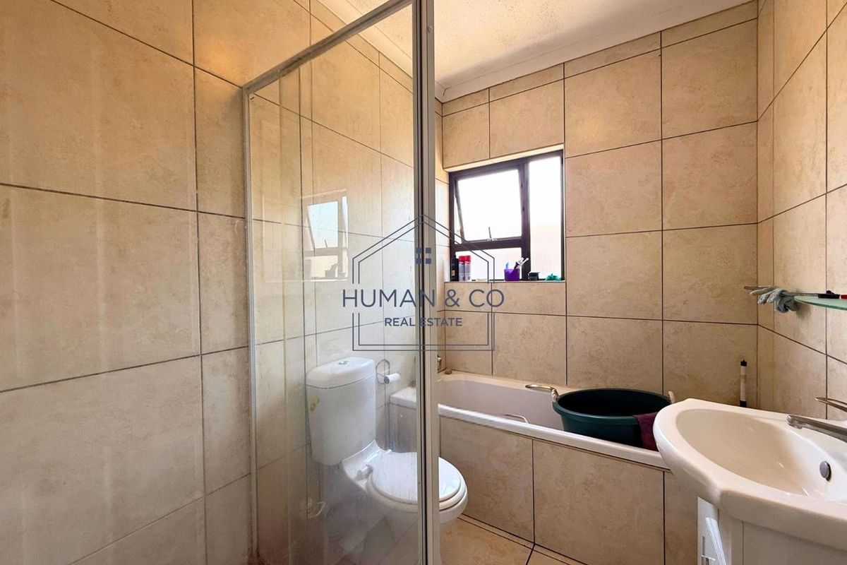 A functional bathroom featuring a combined shower and bathtub unit, tiled walls and flooring, and a pedestal basin.