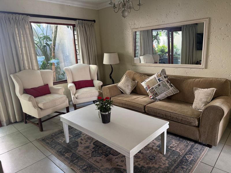 A comfortable living room featuring tiled flooring, textured walls, and a large window providing natural light and garden views.