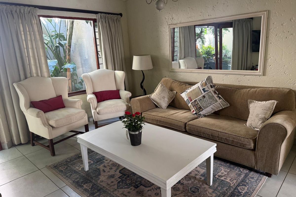 A comfortable living room featuring tiled flooring, textured walls, and a large window providing natural light and garden views.