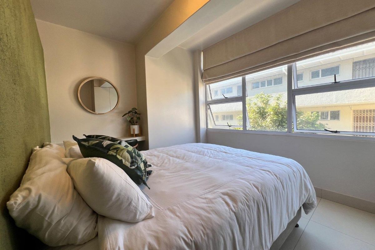 A well-lit bedroom featuring tiled flooring, neutral wall finishes, and large windows with integrated blinds, offering a clean and functional living space.
