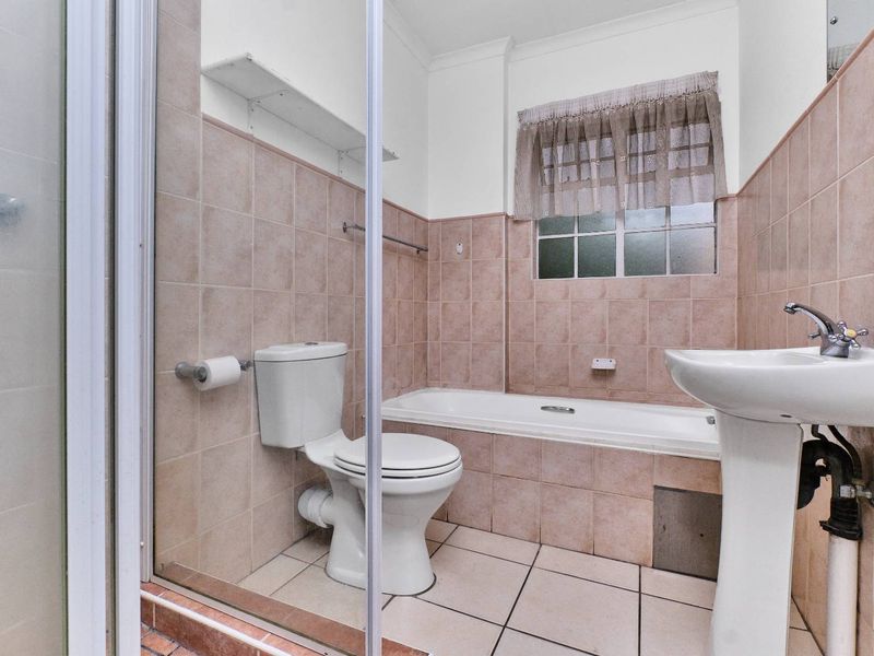 A functional bathroom featuring a pedestal basin, built-in bathtub, and a separate shower enclosure with neutral wall and floor tiling.
