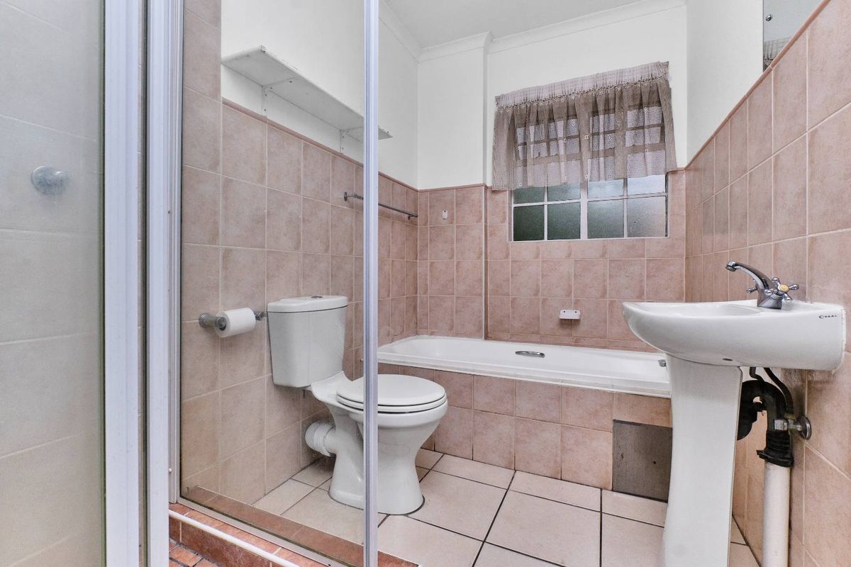 A functional bathroom featuring a pedestal basin, built-in bathtub, and a separate shower enclosure with neutral wall and floor tiling.