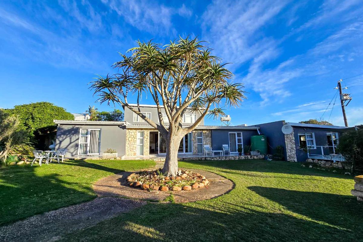 Rear view of the farm property featuring a landscaped garden, mature tree, and stone-clad exterior walls with multiple access points.