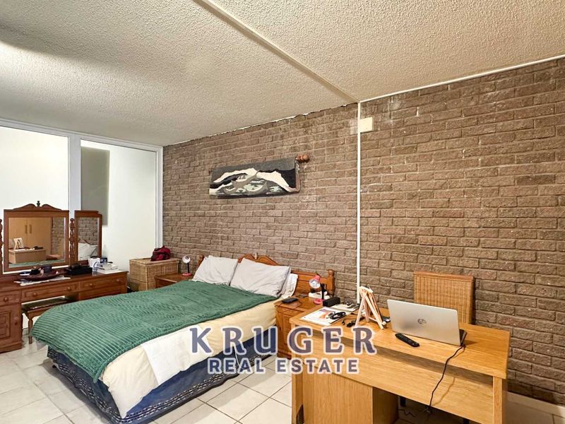 A bedroom featuring an exposed brick wall, tiled flooring, and a sliding glass door, offering a functional space with potential for modern updates.
