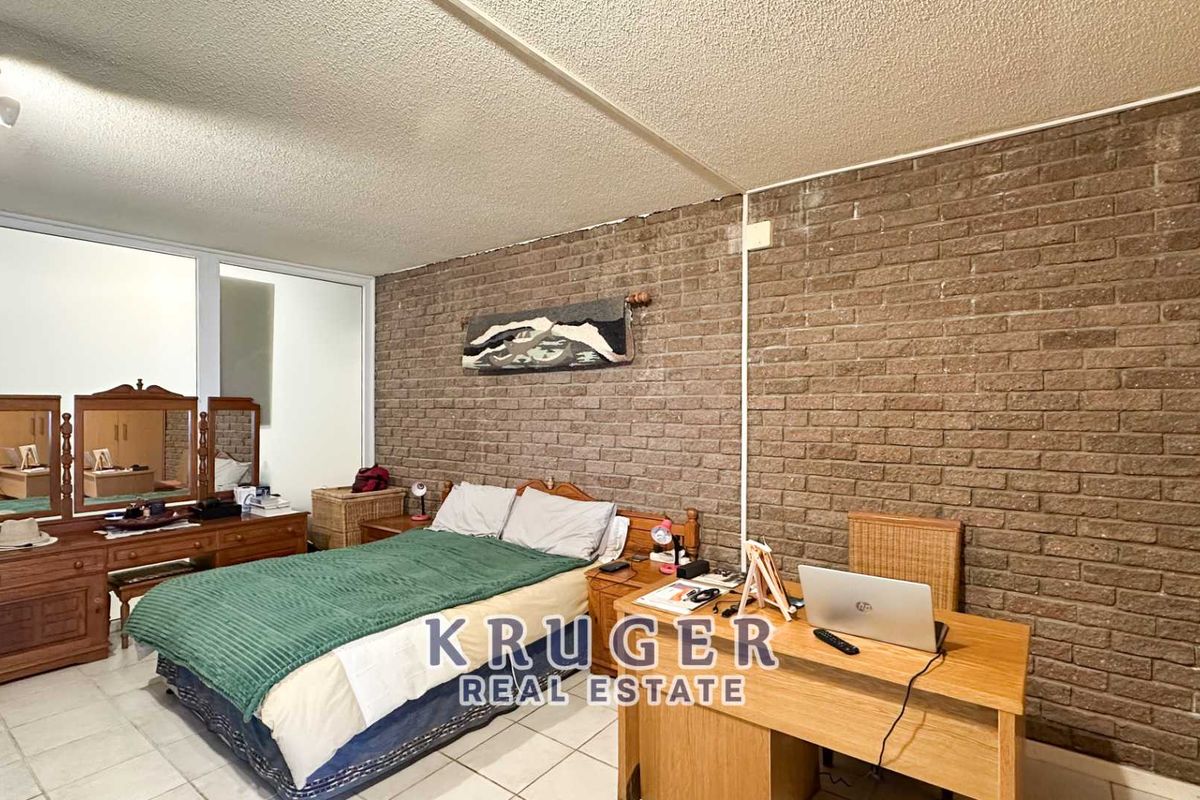 A bedroom featuring an exposed brick wall, tiled flooring, and a sliding glass door, offering a functional space with potential for modern updates.
